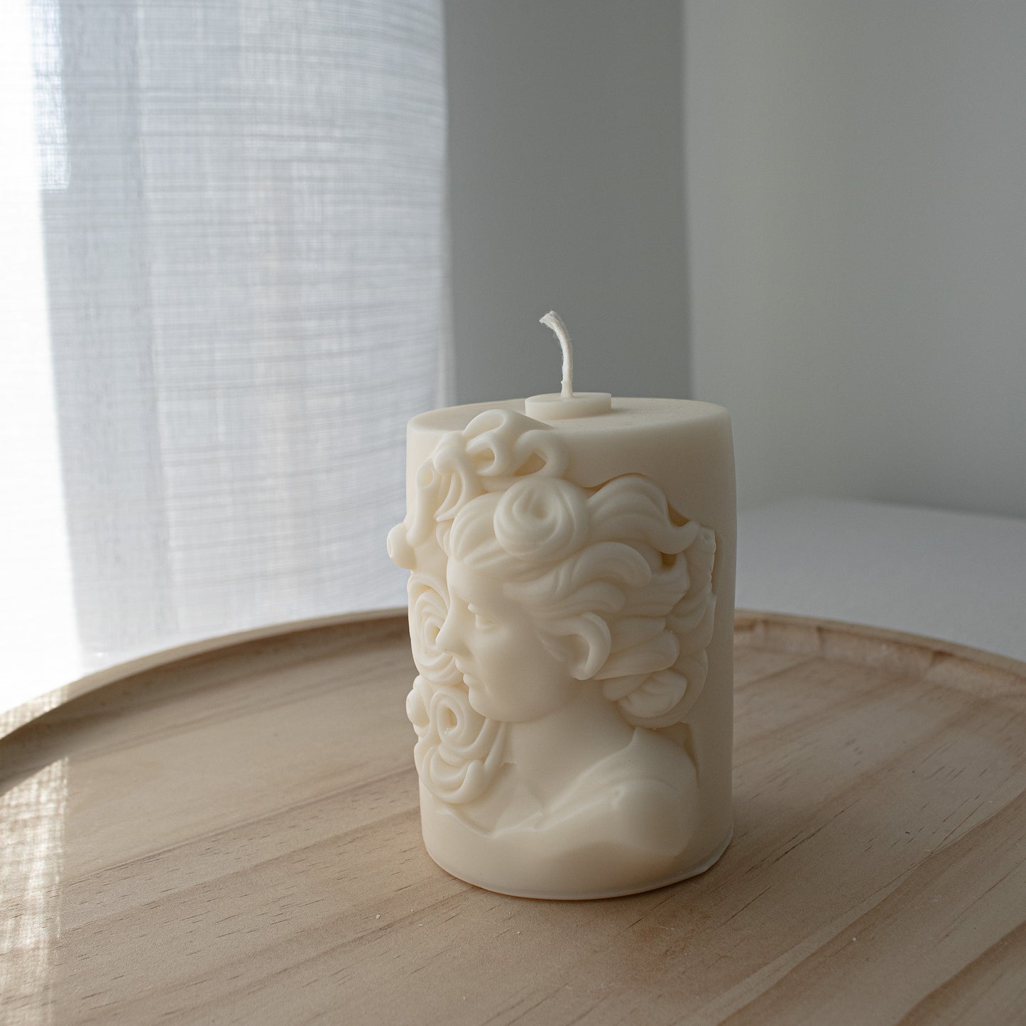 Hellenistic-inspired candle with ornate depiction of a woman’s face and curls
