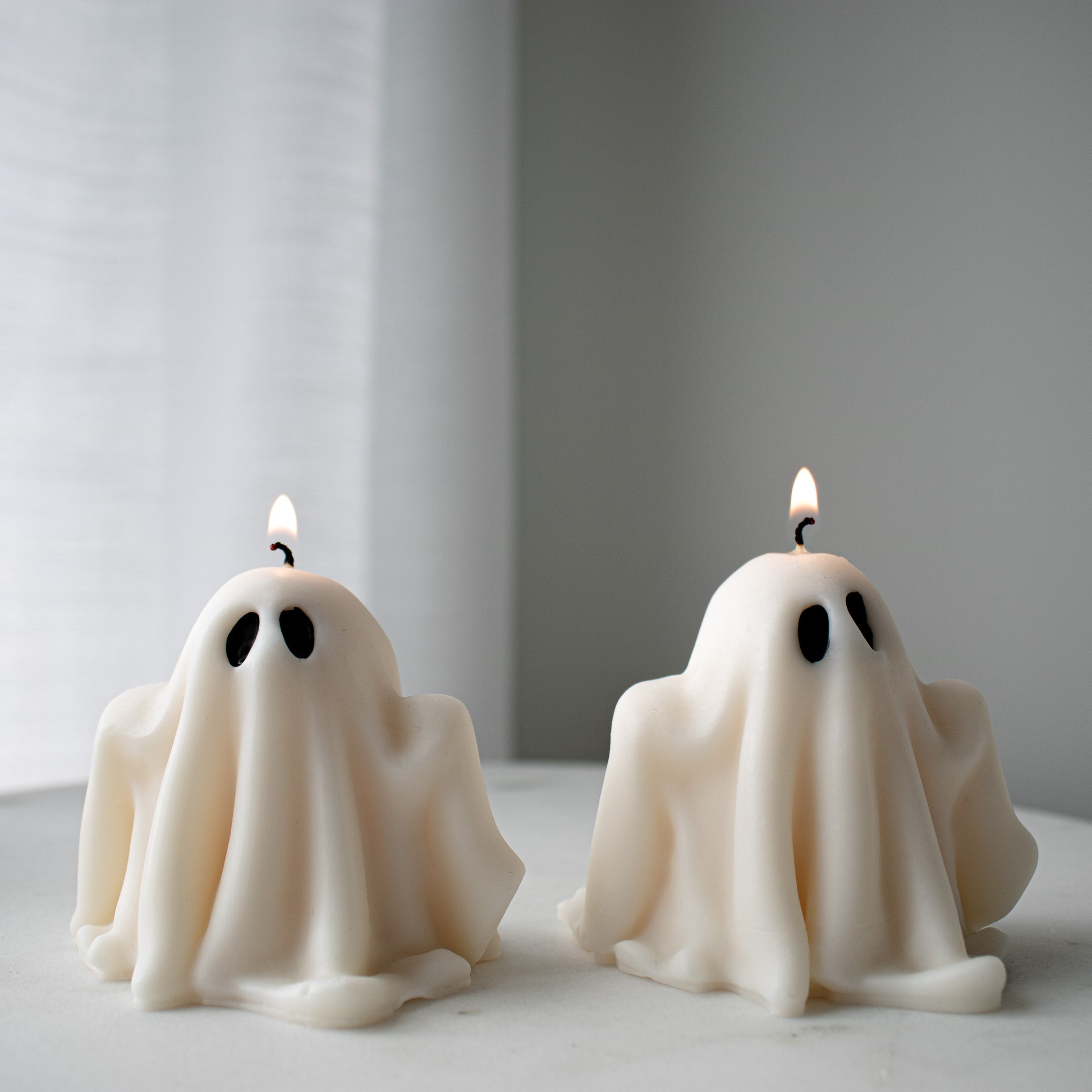 ghost-shaped candles with lit wicks on a neutral background