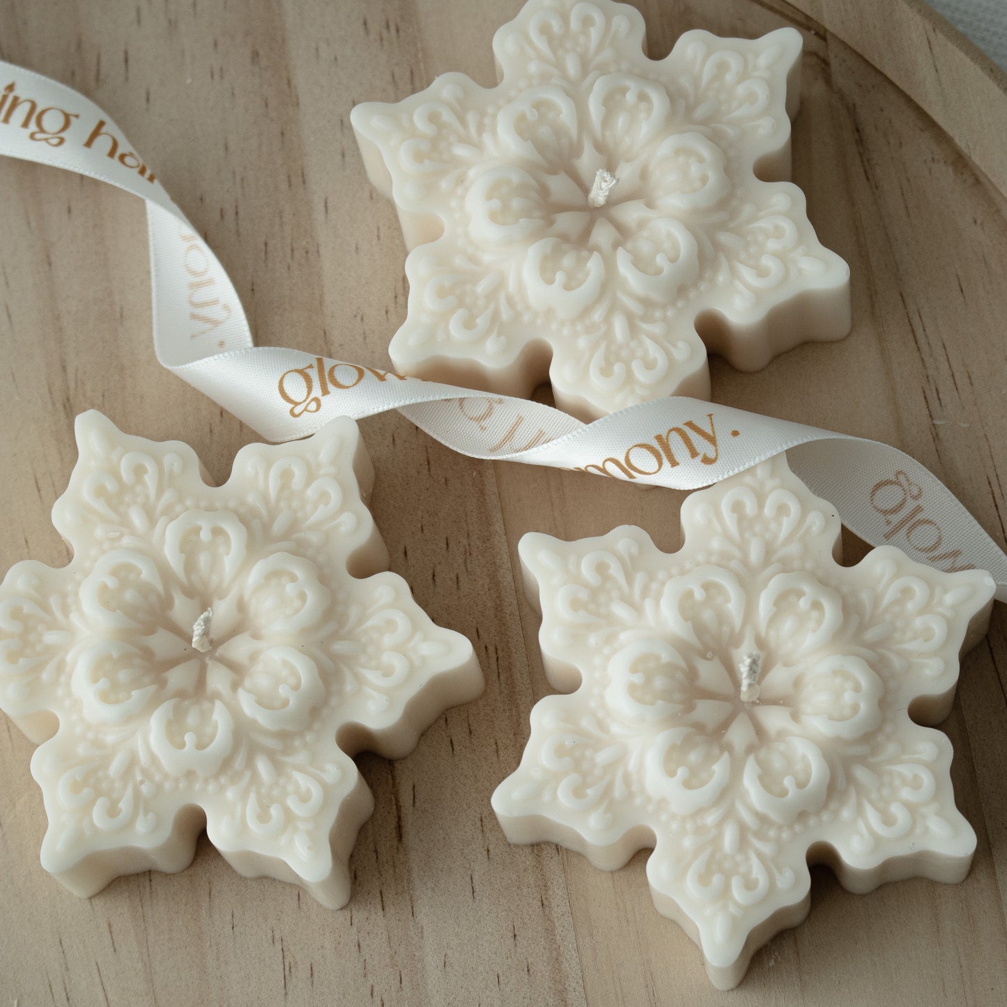 Three snowflake-shaped white ornaments with intricate patterns on a wooden surface, tied together with a ribbon.