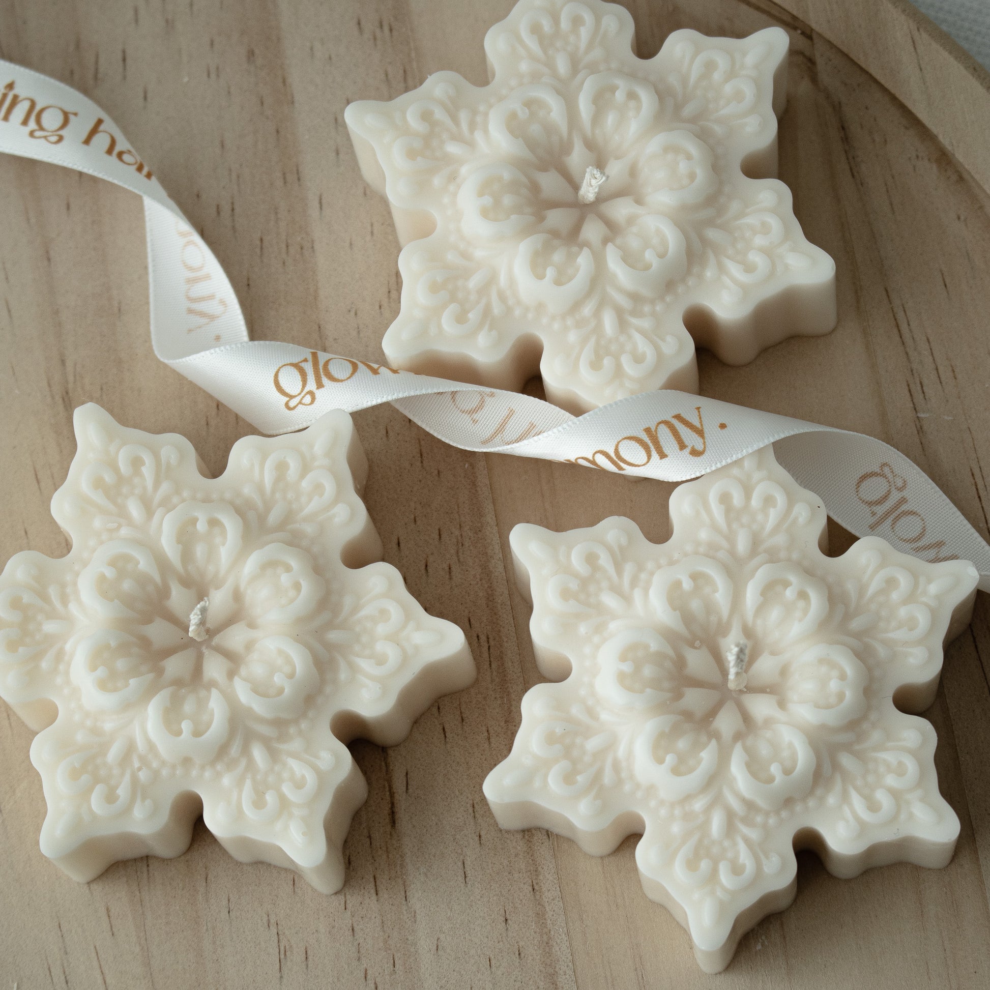 Three snowflake-shaped white ornaments with intricate patterns on a wooden surface, tied together with a ribbon.